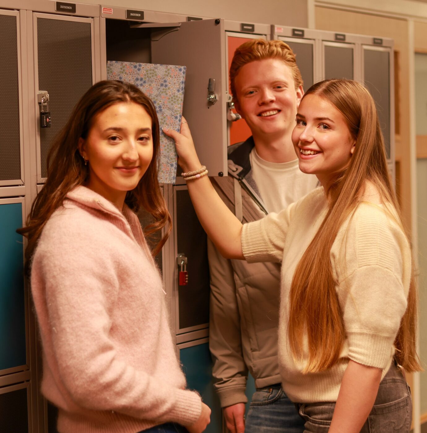 8T1A0093-2-1 Tre elever står ved skapene i en gang, og en av elevene legger en mønstret mappe inn i et skap.
