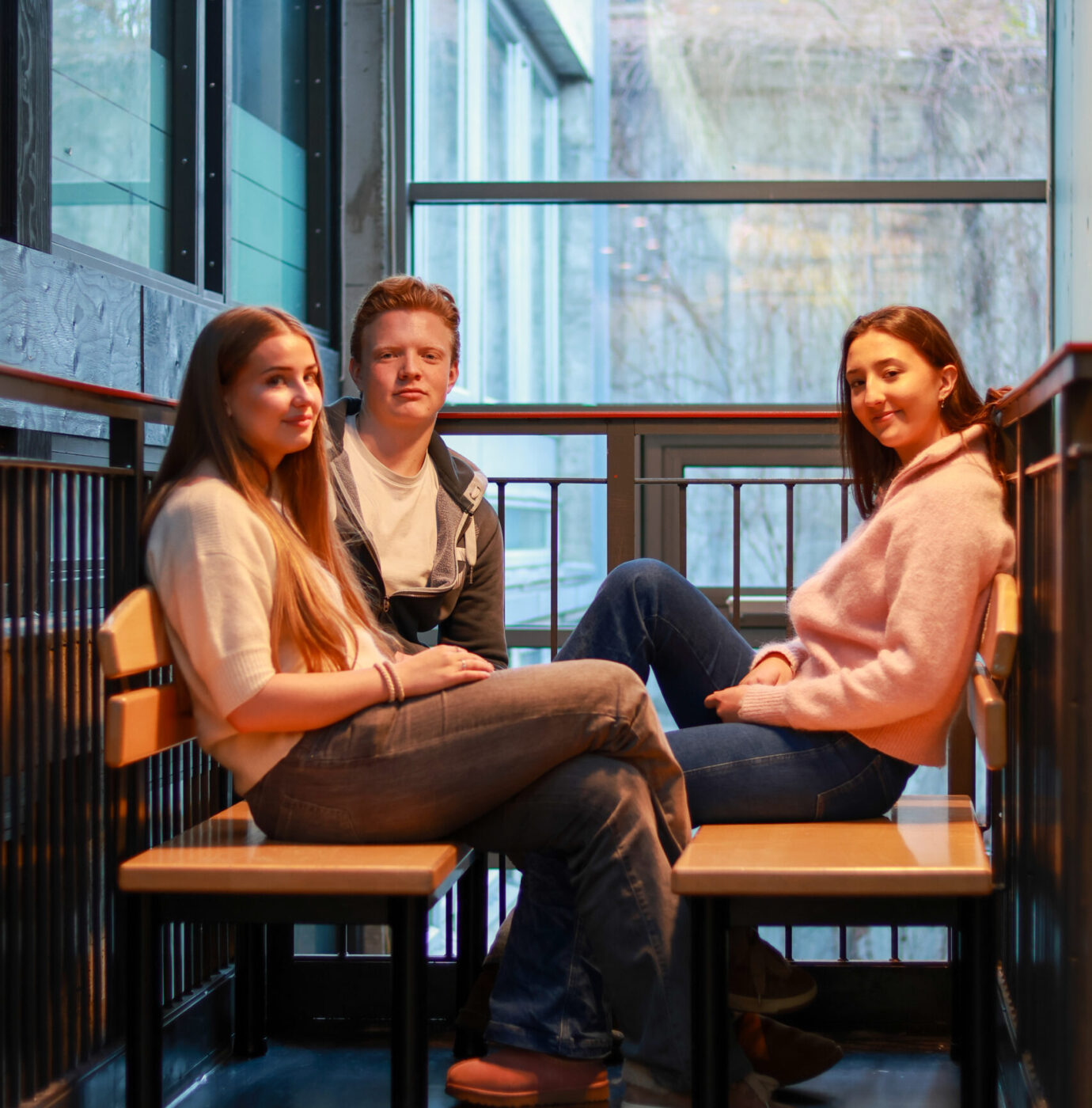 8T1A0116-2 Tre personer sitter overfor hverandre på benker i et moderne rom med glassvegger og naturlig lysinnslipp.