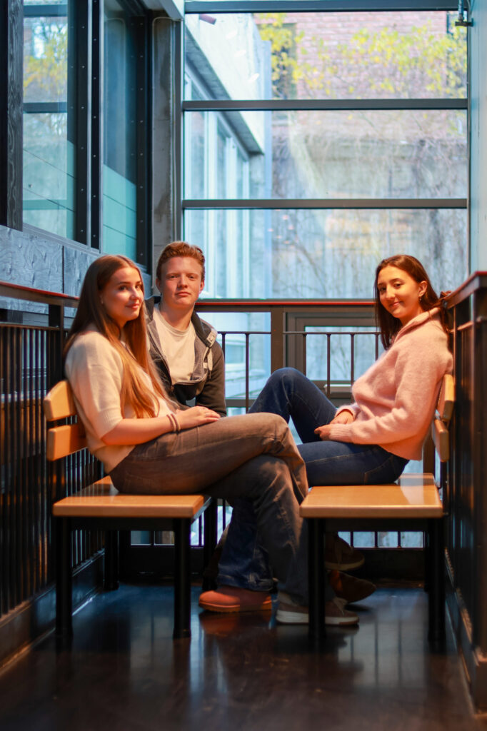 8T1A0116-2 Tre personer sitter overfor hverandre på benker i et moderne rom med glassvegger og naturlig lysinnslipp.