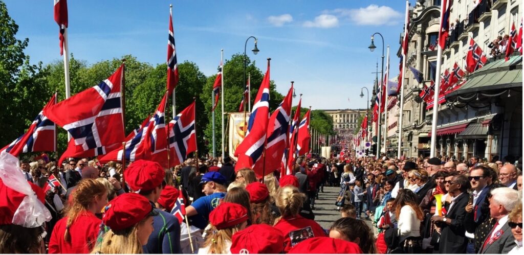 Bilde1 Folkemengder som feirer utendørs med mange norske flagg langs en bygate.