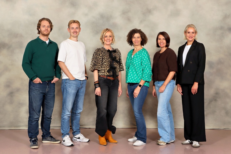 _Gruppebilde Seks voksne står på rekke og rad vendt mot kamera, kledd i uformelle og halvformelle antrekk, mot en nøytral studiobakgrunn.