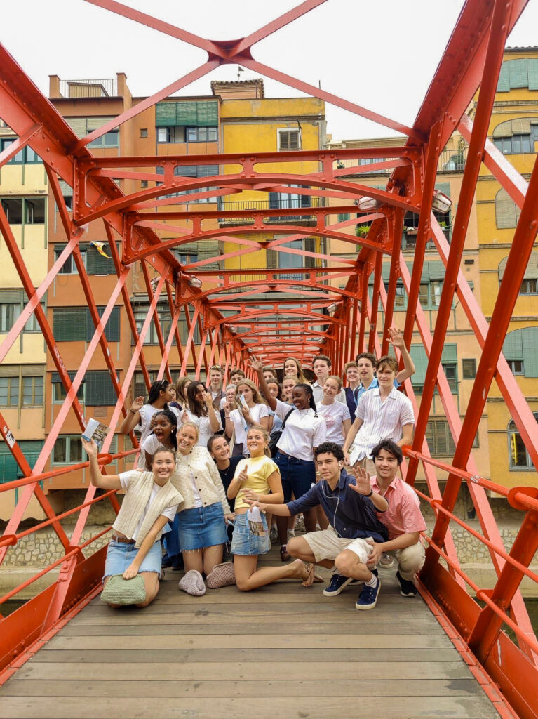 Side 4-5 Barcelona 1 En gruppe unge mennesker poserer for et bilde på en rød metallbro med fargerike bygninger i bakgrunnen.